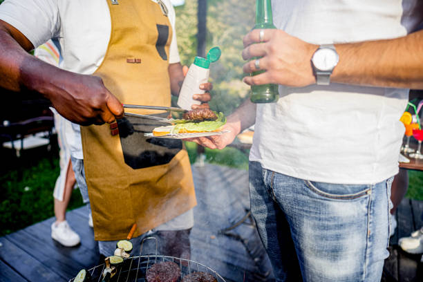 Friends having a barbecue backyard party, a man with an apron grilling and giving meats to his friends