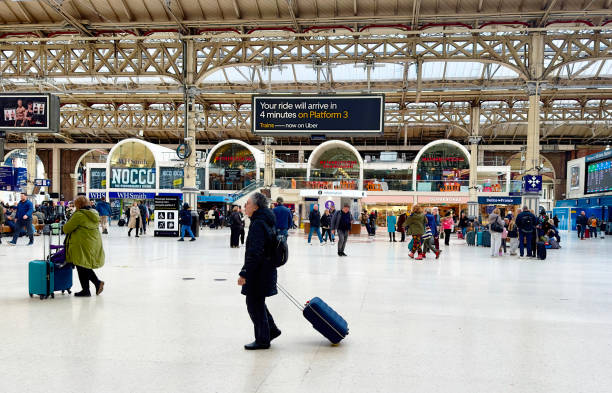 London, UK - March 4, 2024: A man pulling a suitcase with other rail passengers walking across the main concourse at Victoria Station, London, UK.