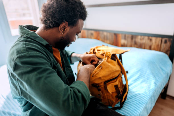 junger lässig gekleideter mann packt rucksack im hotelzimmer aus - cool-pack stock-fotos und bilder