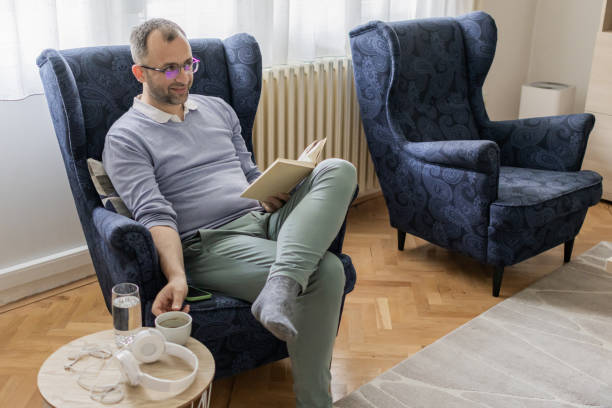 istock Personal development in free time for the weekend. Man is reading book while sitting in an armchair in living room. Man's mental health. 2152318880