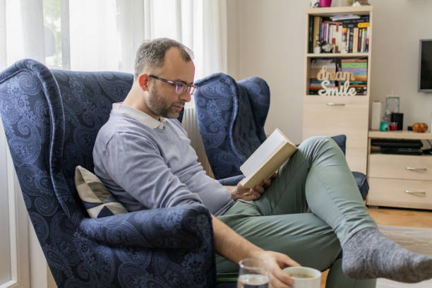 istock Personal development in free time for the weekend. Man is reading book while sitting in an armchair in living room. Man's mental health. 2152319524