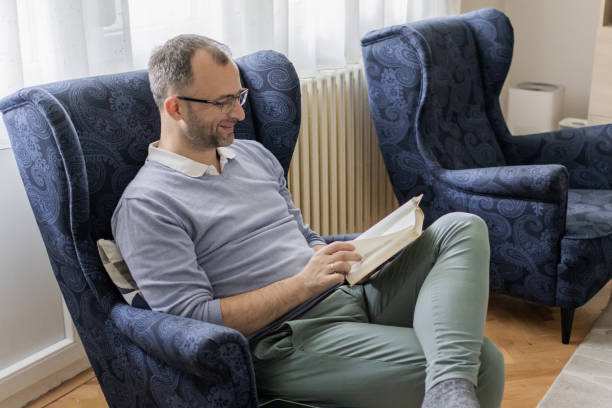 istock Personal development in free time for the weekend. Man is reading book while sitting in an armchair in living room. Man's mental health. 2152319635