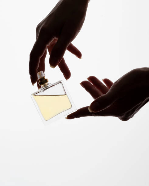 istock Hands elegantly hold a transparent perfume bottle, the golden fluid inside catching the light, all set against a white background. 2152320362