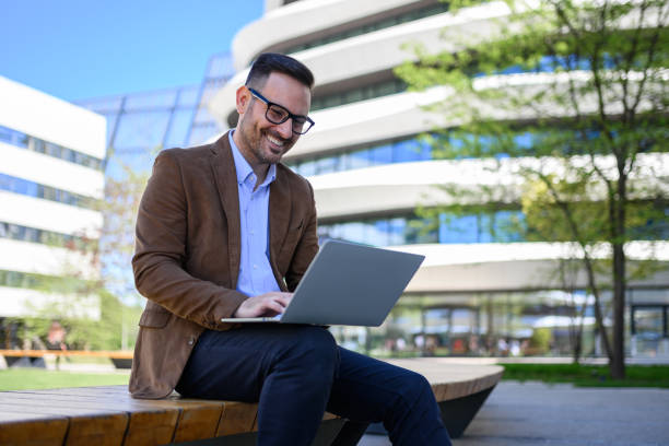 istock Low angle view of happy young man working online over laptop computer while sitting on bench in city 2152325782