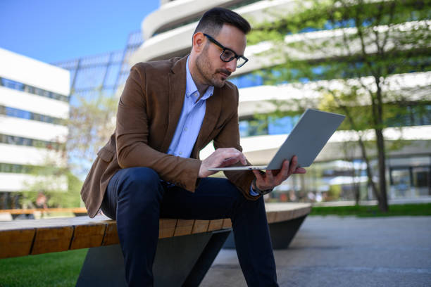 istock Male professional reading e-mails with focus over computer while sitting on bench in modern city 2152325788
