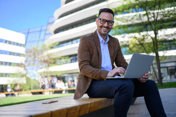 istock Portrait of happy male entrepreneur working on project over wireless computer while sitting on bench 2152325801