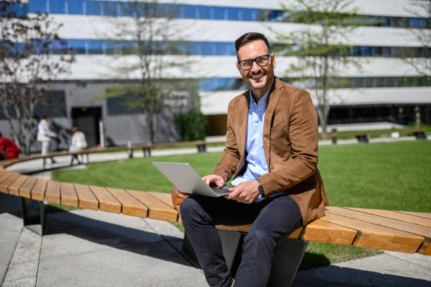 istock Happy young manager working online over computer while sitting on bench against modern building 2152325816