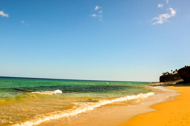 A beautiful beach with a clear blue ocean and a few clouds in the sky. The sky is bright and sunny, and the water is calm. The beach is a perfect place to relax