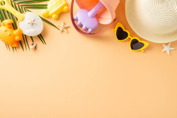 istock Child-friendly beach vacation scene. Flat lay top view composition featuring sand play tools, sunhat, shades, seashells, starfish, palm leaf on pastel orange surface. Text space available 2152338181