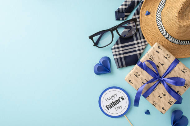 istock Craft heartfelt Father's Day wishes with a top view display featuring a straw hat, classy necktie, gift box, glasses, postcard, and paper hearts on a serene pastel blue backdrop 2152338214