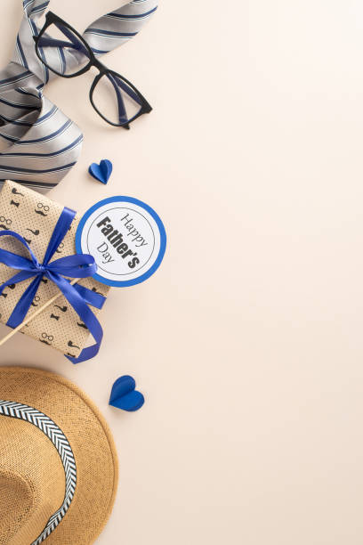 istock Honor Dad on Father's Day with this thoughtful design concept. Vertical top view displays straw hat, sleek tie, giftbox, glasses, postcard, hearts on soft beige backdrop, space for your greeting 2152338245