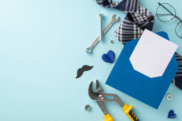 Stylish flat lay of a blue envelope, mustache cut-out, tools, and a striped tie on a pale blue surface perfect for Father's Day or masculine birthday themes