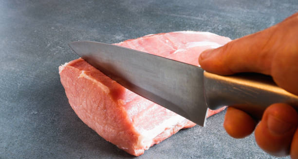 Raw meat. The chef cuts an appetizing chop with a knife on a gray background.