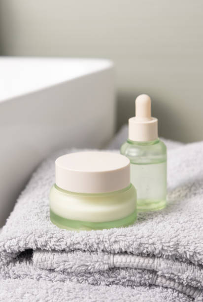 istock Light green dropper bottle and cream jar on light grey bath towel near basin closeup 2152342013