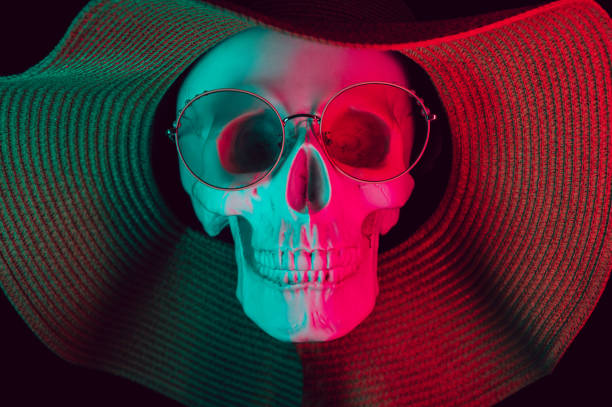 human skull wearing glasses and a hat with colored neon light on a dark background