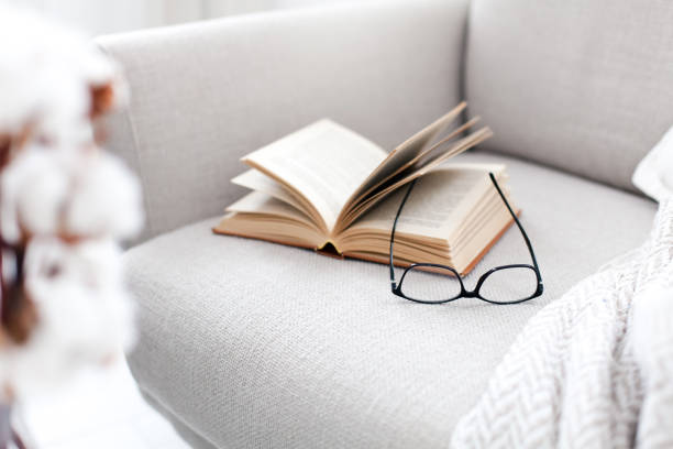 istock Reading book at home. Opened paper pages and spectacles on couch 2152357184