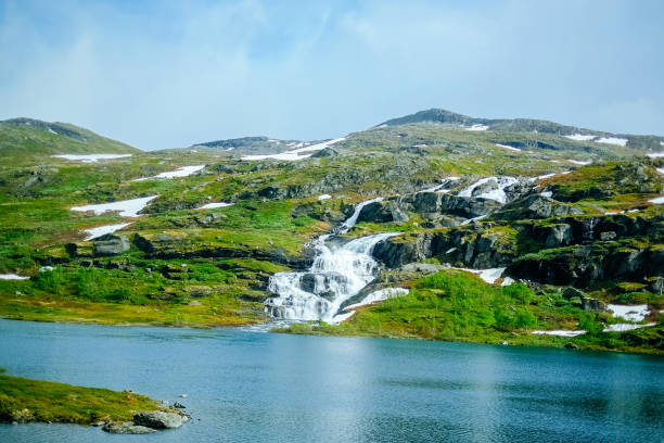 Snowcapped mountains hill and land next to blue lake in Norway