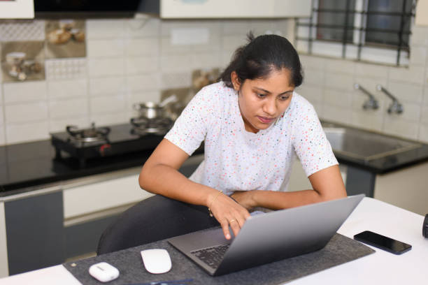 istock indian young woman working with laptop computer in the kitchen at home 2152363041