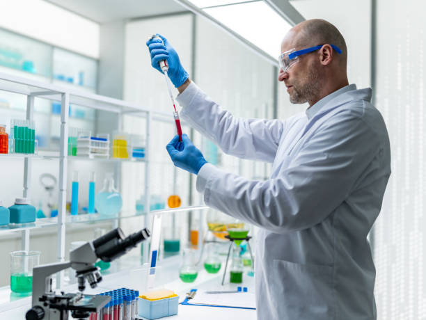 istock Male scientist in lab coat and protective glasses at a laboratory. Taking a blood sample from glass vial with pipette to test under microscope 2152363848