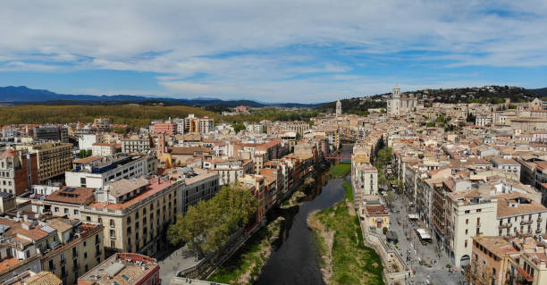 Panoramic view of Girona, Spain, showcasing the colorful houses along the Onyar River. The autumnal trees and cloudy sky add to the charm of this picturesque cityscape