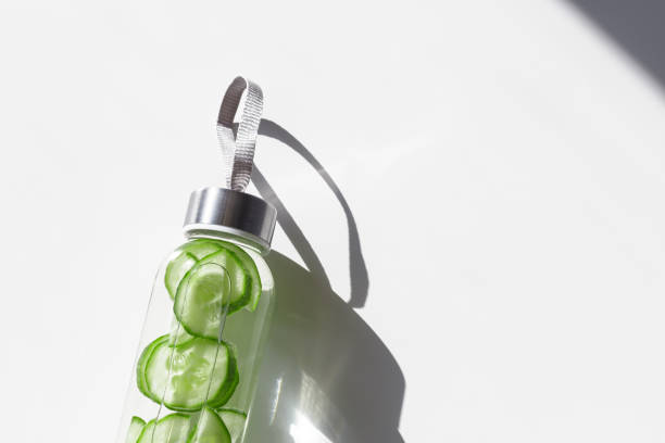 istock Cleansing and refreshing cucumber water drink detox, shadow at sunlight on white with sun glare caustics. Wellness, alkaline diet, eating healthy concept. Stylish glass reusable water bottle 2152407678