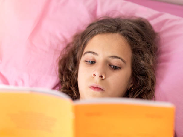 istock Young girl Reading Book in pink Bed 2152424362