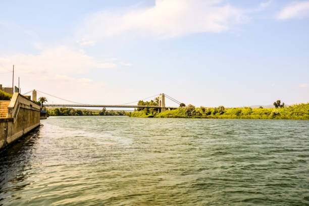 A bridge spans a river, with a green bridge in the foreground. The water is calm and the sky is clear