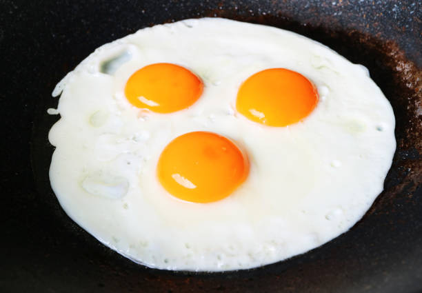 Two eggs frying in a teflon plan.  Olive oil sizzling in pan on stove.   Sunny side up.