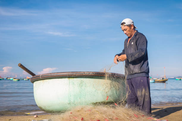 Vietnamese man checking fishing nets, fishing village, Mui Ne, Vietnam. Fishermen's boats on the background.