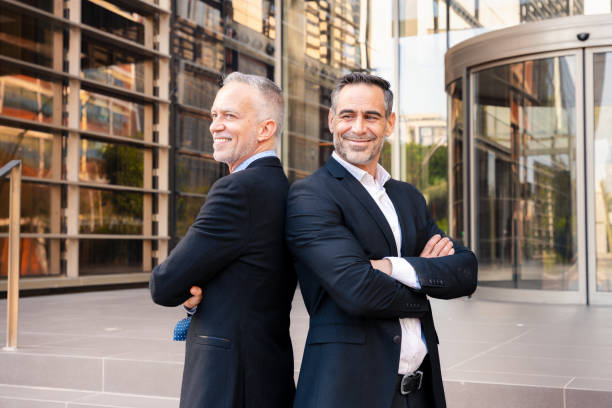 istock Portrait two successful businessmen standing back to back looking at camera, 2152449356