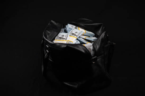 On a black background there is a bag with stacks of hundred dollar bills. A black leather bag full of dollars stands on a black background. Bag with a lot of money. Victory concept, big profit. On a black background there is a bag with stacks of hundred dollar bills. A black leather bag full of dollars stands on a black background. Bag with a lot of money. Victory concept, big profit.. one hundred dollar stamp stock pictures, royalty-free photos & images