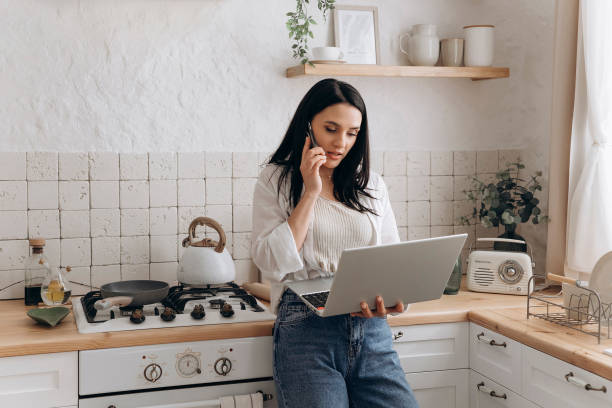 istock Confident young woman freelancer successfully balancing remote work and home chores, talk on the phone call and work on laptop in a well-organized, stylish kitchen. Concept of lifestyle management 2152454188