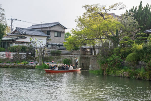 Yanagawa, Japan - April 4, 2024: tourist people and boatman on boat called Donkobune through Castle Moat Water Gate tunnel at spring. Famous travel destination to cruising and sightseeing along river.