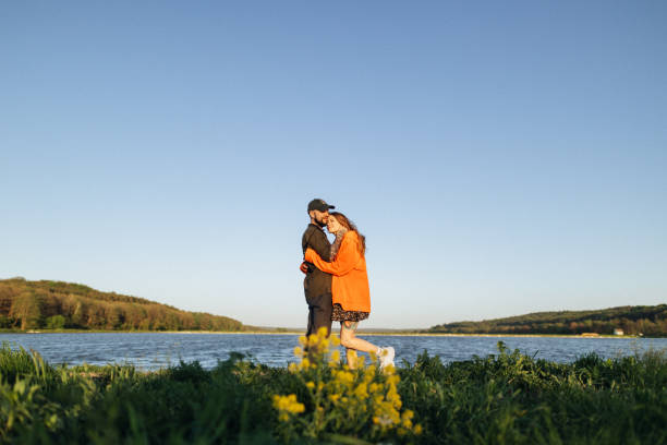 In a scene of pure affection, a loving couple shares a cute embrace against the tranquil backdrop of the lake. Their arms wrapped around each other, they lean in close, cherishing the warmth of their connection amidst the serene beauty of nature