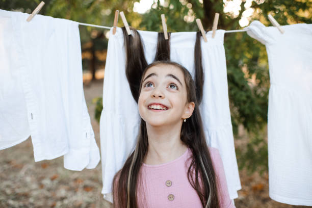 A baby is standing with back to a clothesline with bright colored wet children's clothes drying in the wind
