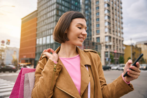 istock Smiling female with paper bags using mobile phone 2152482389