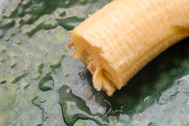 A piece of peeled banana. Close up image of fruit ready to eat. Cut piece on wet green background. Light and healthy snack.