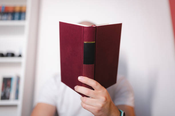 Close-up of an unrecognizable young man holding books with a bookshelf in the background.