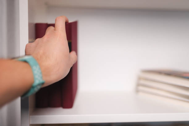 Close-up of a human hand taking a book from the bookshelf.