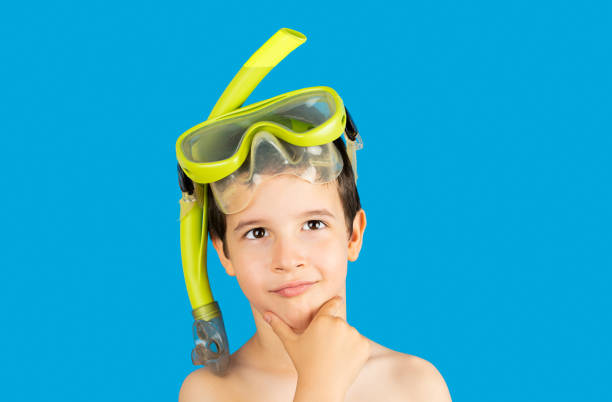Child with mask tuba and snorkel with hand on chin thinking about question, thoughtful expression.Concept of doubt and looking aside. Snorkeling, swimming, vacation concept isolated on blue background.Caucasian male model