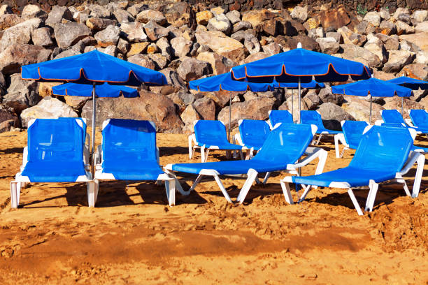 Sunbeds and umbrellas on the sandy beach with rocks. Blue sun loungers