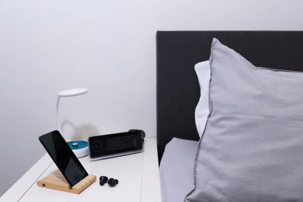 istock Smartphone on the bedside table with headset, lamp,  clock and bed as background 2152518204