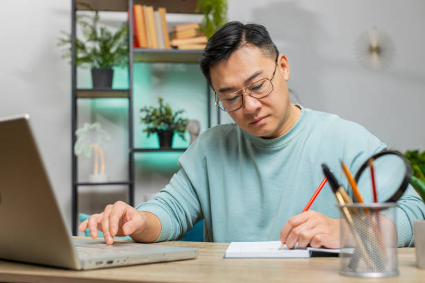 istock Asian man freelancer making notes on notebook at home, use laptop, prepare business financial report 2152519115