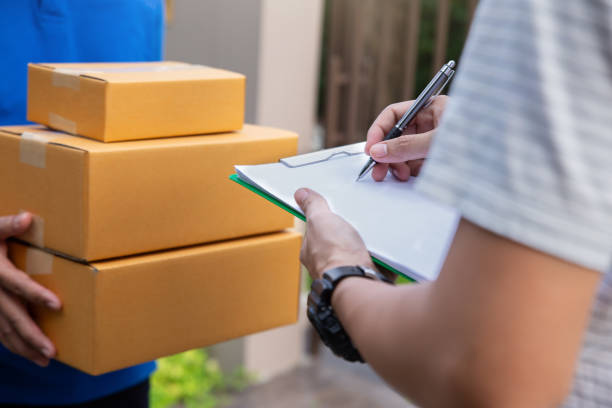 istock Delivery man holding a cardboard box while young man putting signature in clipboard. 2152537875