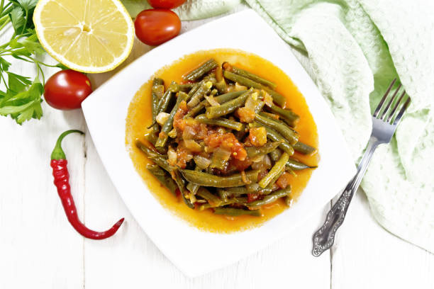 Arabic dish Ful green bean stew with tomatoes, onions, spices and lemon in bowl, napkin on top of wooden board background from above