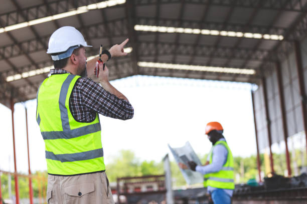 istock A senior civil engineer is seen from behind while working at a construction site. They are holding a walkie-talkie and overseeing the work progress. 2152544178