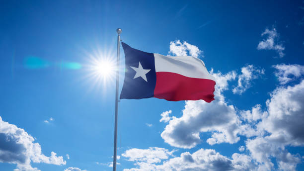 Texas flag waving on pole, bright sun in the blue summer sky on the background