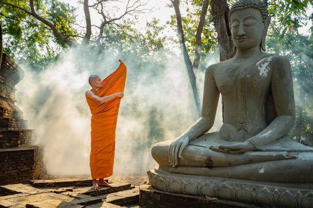 A monk is wearing a robe near a Buddha image.