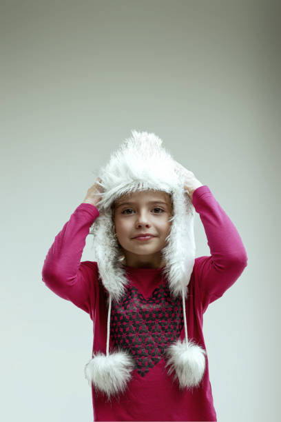 Enthusiastic young girl in a pink sweater and white fur hat shows her excitement for the holiday season with a bright smile