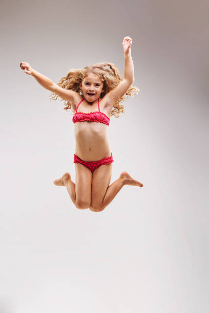 Little girl in pink swimsuit jumps so much that she seems to be flying through the air, with her curly blond hair around her. Proud and strong.